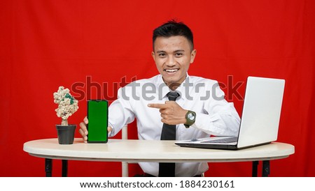Young asian business man pointing handphone green screen isolated red background