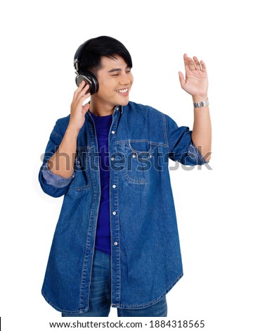 Young asian man dance, swaying, and lifting his arms rhythmically while listening to the music from headphone. Portrait on white background with studio light.