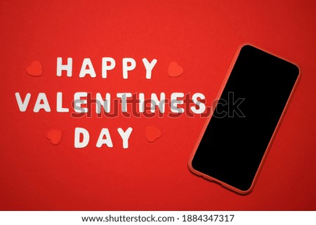 Happy Valentine's Day greeting card with hearts and phone with blank screen on red background. Top view with space for your greetings or smart phone app. Love texting and online dating concept.