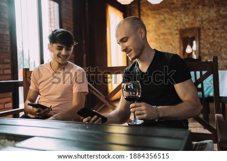 Two friends sitting on a restaurant bench and using their cell phone, choosing images for the social media application.