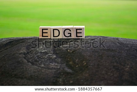 Edge text on wooden cube block on top of big stone with blurred background