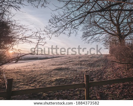 A frozen misty field at sunrise. The layers mist settle over the lower ground across a classic British countryside view at sunrise in winter.