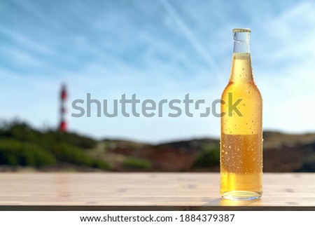 Single bottle of cold beer standing on wooden bar. Dewy glass bottle with blank white label in back light. Relax on beach concept, alcoholic drinks and refreshment concept.