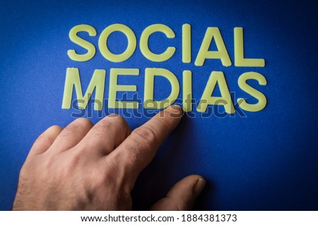 Human finger pointing the words Social Medias written with plastic letters on blue paper background, concept