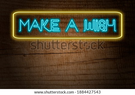 neon illustration with the legend make a wish, with a wooden background and copyspace to fill in