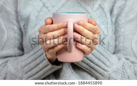 Female hands holding a pink cup against a knitted grey sweater.