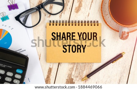 Notebook with the text SHARE YOUR STORY on the office table among the stationery.