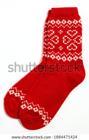 A pair of warm woolen winter socks with knitted white decorations, hearts isolated on white background. Socks for Christmas, holiday time or cold winter. Red and white color