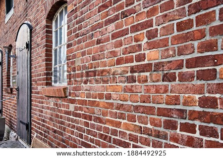 Oblique view of a red old weathered brick wall with a blurred window at the end Royalty-Free Stock Photo #1884492925