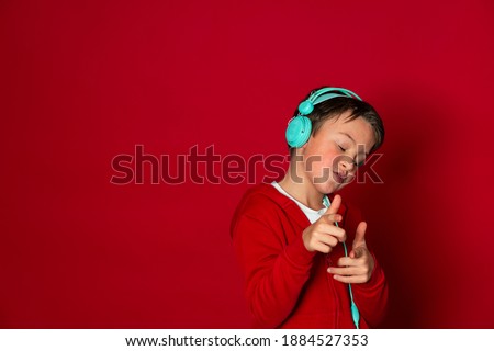 young cool schoolboy with turquoise headphones and red sweater is posing