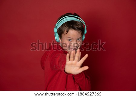 young cool schoolboy with turquoise headphones and red sweater is posing