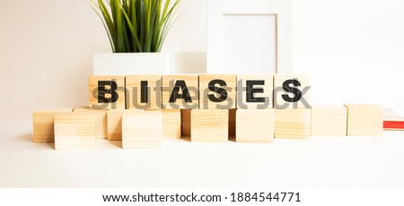 Wooden cubes with letters on a white table. The word is BIASES. White background with photo frame, house plant.