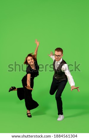 Rock n roll. Old-school fashioned young woman dancing isolated on green studio background. Artist fashion, motion and action concept, youth culture, fashion returning. Young stylish man and woman.