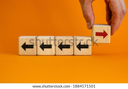 Hand holding wooden block with red arrow facing the opposite direction black arrows. Unique, think different, individual and standing out from the crowd concept