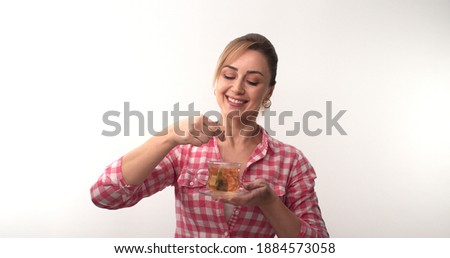 Young happy woman on a white background, holding in hand hot black tea bag. Peaceful woman sniffing tea smiles at camera.