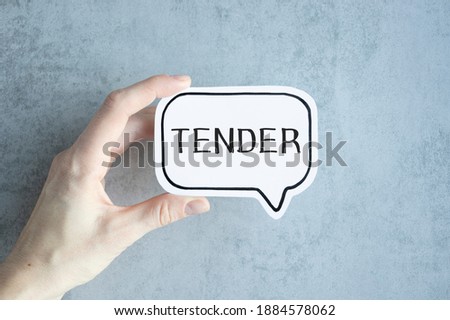 Sticker with text Tender on a white paper holding by a man in suit. Unfocused background.