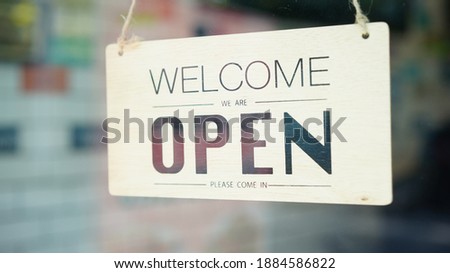 Open and closed flip sign in front of coffee shop and restaurant glass door. Wooden sign of place's status. Say sorry we're closed. Please come back again and another side is Welcome we're closed.