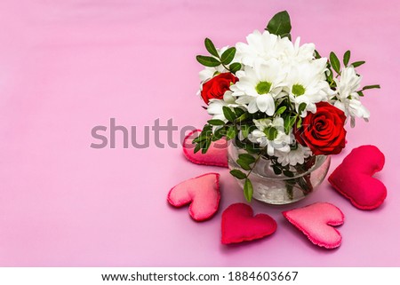A bouquet of fresh flowers in glass vase and soft felt hearts. Valentine's day or Wedding concept. Gentle pink textured background