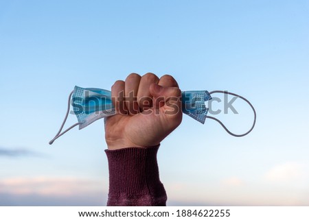 Man holding used medical mask on clear sky background. End of coronavirus pandemic and back to normal life again. Copy space. Coronavirus stop concept, after COVID-19. Royalty-Free Stock Photo #1884622255