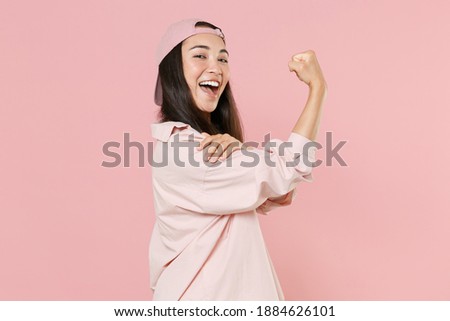 Side view of strong young asian woman 20s in casual clothes cap posing isolated on pastel pink background studio portrait. People emotions lifestyle concept. Mock up copy space. Showing biceps muscles Royalty-Free Stock Photo #1884626101