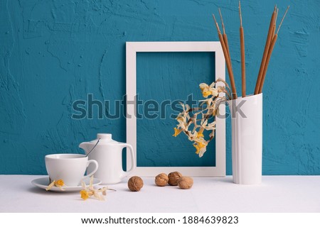 white vase with reed cones, photo frame, walnuts, coffee cup and teapot on a blue background on the table