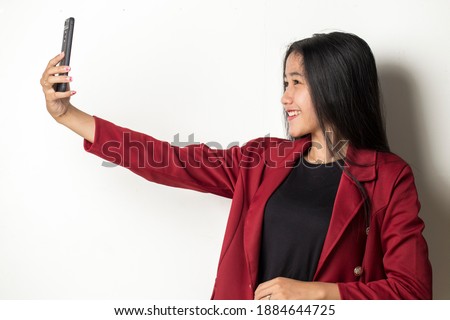 Happy Asian business woman with mobile phone making selfie. Portrait of smiling girl, posing on white background
