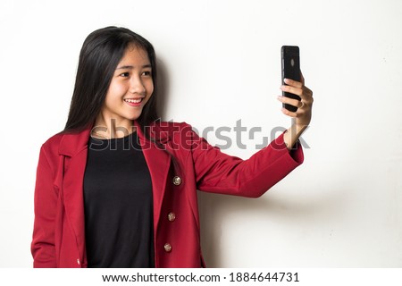 Happy Asian business woman with mobile phone making selfie. Portrait of smiling girl, posing on white background
