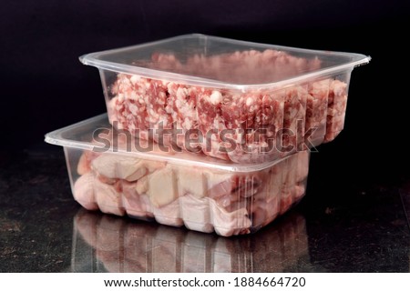 ransparent resealable vacuum plastic trays filled with fresh raw minced meat and pieces of raw chicken. Food delivery concept. Black background. Selective focus Royalty-Free Stock Photo #1884664720