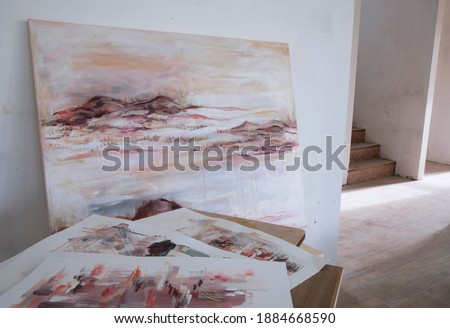 Contemporary art. Interior decoration and lifestyle. Selective focus on a modern painting depicting the ocean and rocky shore at sunset. The stairs and empty house in the background.