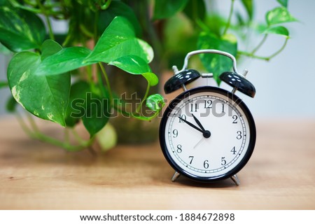 Desktop retro alarm clock on green plant background. Wooden table.