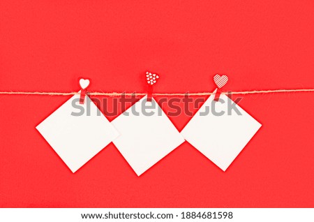 three white empty square stickers for notes pinned to rope with clothespin with hearts on red background, valentines day concept, greeting card