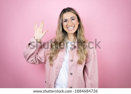 Young beautiful blonde woman with long hair standing over pink background doing hand symbol