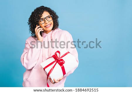 Happy african american curly lady in casual laughing while holding present isolated over blue background. Using phone. 