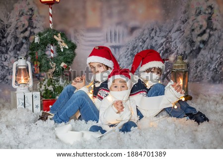 Children, sitting in the snow, wrapped in toilet paper and christmas light strings, looking at camera