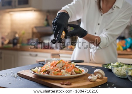 Close up portrait of chef hands pouring olive oil on a fresh salad. Chef wearing protective gloves.