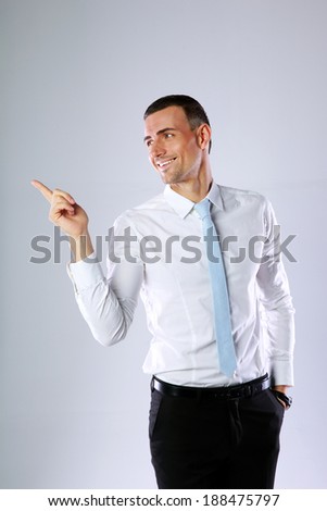 Happy businessman pointing at something on gray background