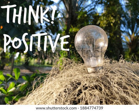 Selective focus.Text Think Positive with bulb on net with blur green flora background.Business concept idea.Shot were noise and film grain in full resolution.
