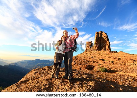 Couple taking selfie hiking in beautiful nature with smart phone. Happy couple walking enjoying view and taking pictures with smartphone. Man and woman by Roque Nublo, Gran Canaria, Canary Islands.