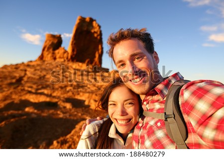 Happy couple taking selfie self-portrait photo hiking. Two friends or lovers on hike smiling at camera outdoors mountains by Roque Nublo, Gran Canaria, Canary Islands, Spain.
