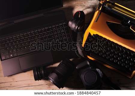 Photographic and office equipment for photojournalists with vintage typewriter, laptop, camera and photographic lenses on a desk in an overhead shot from top to bottom Royalty-Free Stock Photo #1884840457