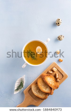 Bouillon in white round soup bowl, quail egg and fennel leaf on blue background. Toasted bread on wooden board. Flat lay. Vertical orientation. Homemade healthy eating and dieting concept. Copy space.