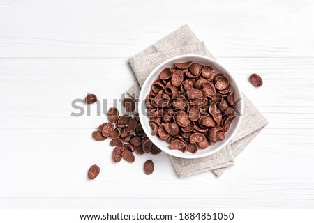 Top view of bowl with sweet chocolate cereal flakes for breakfast on white wooden background Royalty-Free Stock Photo #1884851050