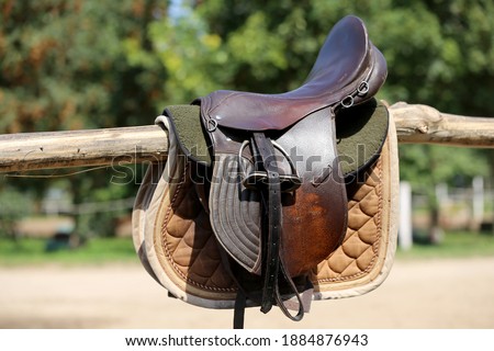 Old leather saddle with stirrups for show jumping race Saddle on a back of a sport horse. Equestrian sport event background Royalty-Free Stock Photo #1884876943
