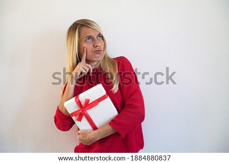 Young woman hold gift box white color with red tape. Person deep thinking and in thought with delight. Girl wearing red blouse on white background. In Lovely Valentine day in 14th February get a gift.