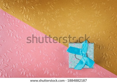 Small blue gift box. Minimal composition on gold and pink background.