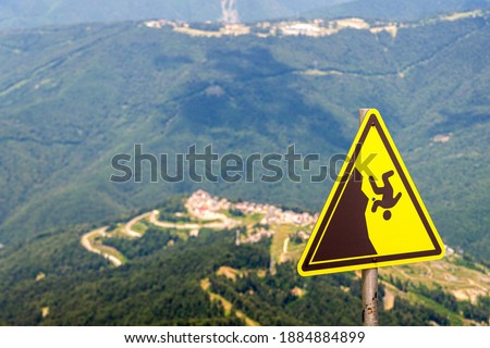 Yellow warning sign with symbol of man falling. In the background a large summer mountains, rocks