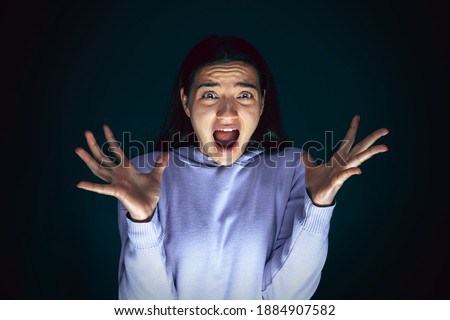 Screaming. Portrait of young crazy scared and shocked caucasian woman isolated on dark background. Copyspace for ad. Bright facial expression, human emotions concept. Looking horror on TV, cinema.