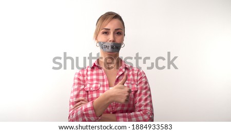 Young woman with mouth taped writing stay home. Woman with tape on her mouth with home message over white background. Message given silently. Stay at home.