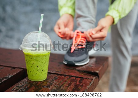 Green detox smoothie cup and woman lacing running shoes before workout on rainy day. Fitness and healthy lifestyle concept. Royalty-Free Stock Photo #188498762