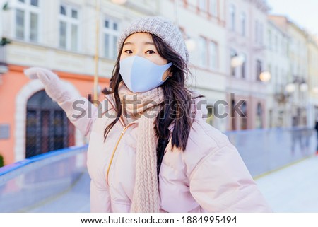 Positive emotion active lifestyle. Asian woman wearing mask for protect pm2.5 and Covid-19 virus outdoor at european city on the ice rink trying ride on ice skates in sunny frozy day.